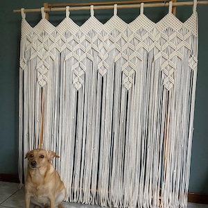 May include: A large, white macrame wall hanging with a geometric pattern. The hanging is made of thick cotton cord and is attached to a wooden dowel rod.