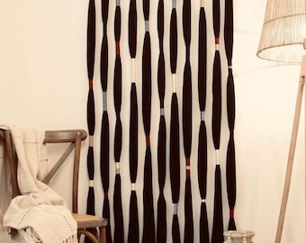 May include: A black and white wall hanging with a series of vertical, elongated shapes. The shapes are black with sections of red, gray, and white. The wall hanging is mounted on a wooden rod. The text "SN HANDICRAFTS" is visible at the top.