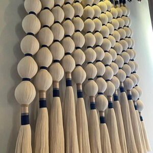 May include: A large wall hanging featuring rows of cream-colored, spherical shapes with navy blue accents. Long, cream-colored tassels hang below each sphere. The wall decor is made of natural fibers and adds texture to any space.