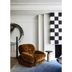 May include: A low-profile armchair upholstered in brown textured fabric with a rounded, plush silhouette. The chair features a metal frame structure visible at the base and sides, providing a distinct contrast to the soft, deep brown upholstery.