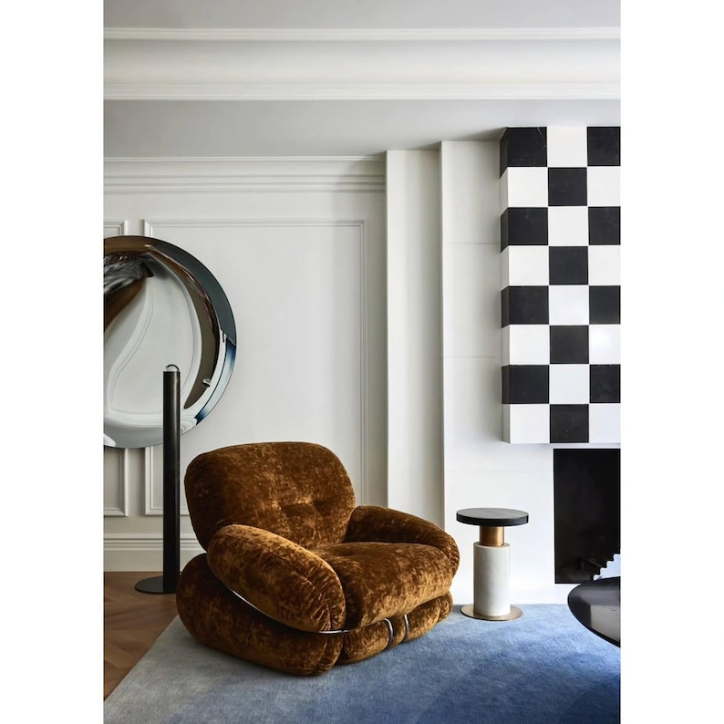 May include: A low-profile armchair upholstered in brown textured fabric with a rounded, plush silhouette. The chair features a metal frame structure visible at the base and sides, providing a distinct contrast to the soft, deep brown upholstery.