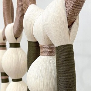 Puede incluir: Primer plano de un tapiz de macram&eacute; con hilo blanco y marr&oacute;n. El tapiz presenta una serie de nudos y bucles, creando un dise&ntilde;o texturizado y org&aacute;nico.