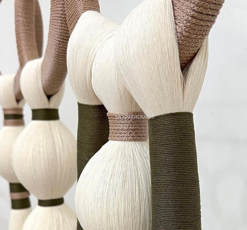 Puede incluir: Primer plano de un tapiz de macram&eacute; con hilo blanco y marr&oacute;n. El tapiz presenta una serie de nudos y bucles, creando un dise&ntilde;o texturizado y org&aacute;nico.