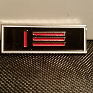 Peut inclure: Une épingle en émail noir et argent avec une ligne rouge verticale et trois lignes rouges horizontales.