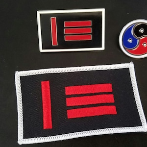 May include: Three pins and a patch are displayed on a black surface. The patch and one pin feature a black background with a red vertical line and three horizontal lines. The other pin is a yin-yang design with blue, black, and red colors.