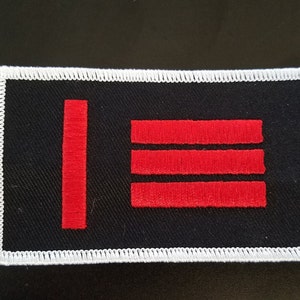 Könnte beinhalten: Ein schwarzer Stoff-Patch mit weißem Rand. Der Patch hat drei rote horizontale Streifen und einen roten vertikalen Streifen.