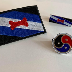Peut inclure: Trois épingles en émail représentant un os rouge sur un fond rayé bleu, blanc et noir, un os rouge sur un fond rayé bleu, blanc et noir et un symbole yin yang rouge et bleu.