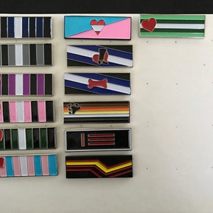 Könnte beinhalten: Eine Sammlung von 11 Emaille-Pins mit verschiedenen Pride-Flaggen, darunter die Transgender-Flagge, die Lesben-Flagge, die Bisexuelle-Flagge, die Pansexuelle-Flagge, die Asexuelle-Flagge, die Genderqueer-Flagge, die Intersex-Flagge, die Non-Binary-Flagge, die Polyamore-Flagge, die Aromantische-Flagge und die Genderfluid-Flagge.