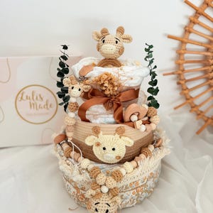 Windeltorte mit gehäkelter Giraffe in beigen Erdtönen, dekoriert mit Holzperlen und Schleife, Geschenkidee für Babyshower oder Taufe.
