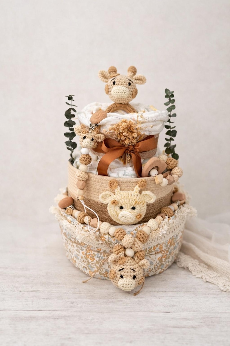 K&ouml;nnte beinhalten: Ein mehrst&ouml;ckiger Babygeschenkkorb mit Giraffen-Motiv. Der Korb enth&auml;lt geh&auml;kelte Giraffen, Holzperlen und ein braunes Band. Er ist mit Windeln und anderen Babyartikeln gef&uuml;llt. Das Farbschema ist neutral mit Beige- und Braunt&ouml;nen.