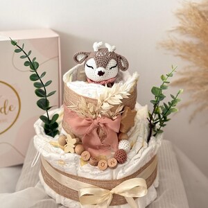 Peut inclure: Un g&acirc;teau &agrave; couches &agrave; deux &eacute;tages d&eacute;cor&eacute; d'un jouet en crochet en forme de cerf, d'un ruban en toile de jute, de lettres en bois qui &eacute;pellent "MOM" et d'autres &eacute;l&eacute;ments naturels.
