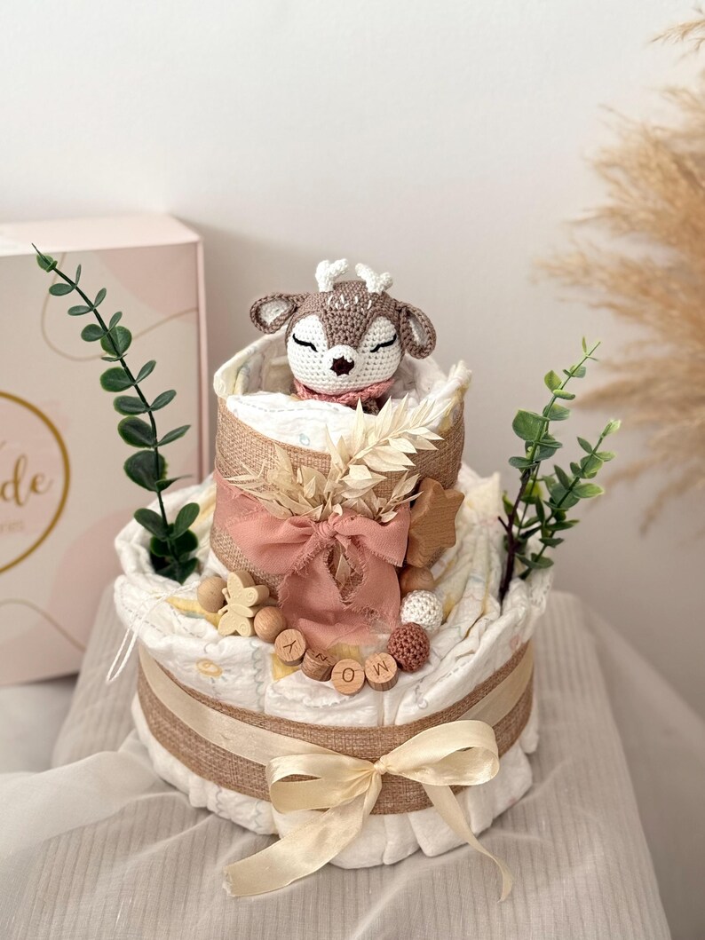 Peut inclure: Un g&acirc;teau &agrave; couches &agrave; deux &eacute;tages d&eacute;cor&eacute; d'un jouet en crochet en forme de cerf, d'un ruban en toile de jute, de lettres en bois qui &eacute;pellent "MOM" et d'autres &eacute;l&eacute;ments naturels.