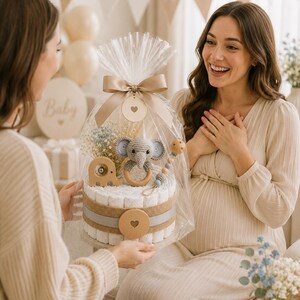 May include: A baby shower gift presented to a pregnant woman. The gift is a diaper cake decorated with a crocheted elephant, wooden accents, and wrapped in cellophane with a bow. The background includes balloons and a banner.