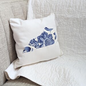 May include: A white throw pillow with a blue and white floral design on a white couch.