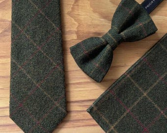 May include: A dark olive green necktie, a pre-tied bow tie, and a pocket square, all featuring a textured wool-like finish with a subtle red and brown grid pattern. The bow tie includes a dark strap with the visible text PRIORY.
