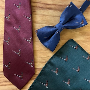 May include: A set of three neckties featuring a pheasant pattern. The ties are in burgundy, navy blue, and forest green.
