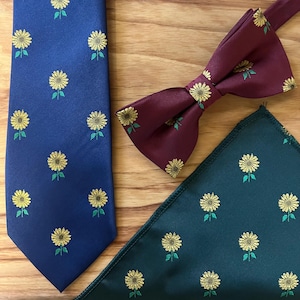 Puede incluir: Un conjunto de tres corbatas con un patrón de girasol. Las corbatas son azul marino, burdeos y verde oscuro.
