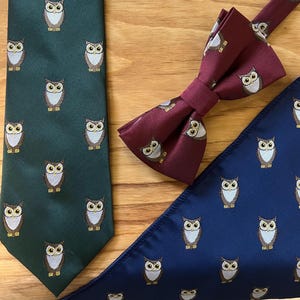 Puede incluir: Un conjunto de tres accesorios para el cuello con un patrón de búho repetido. Una corbata verde, una pajarita burdeos y un pañuelo de bolsillo azul marino.
