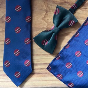 May include: A set comprising a blue tie, a green bow tie, and a blue pocket square. Each item features a repeating pattern of red and white striped circles. The fabric has a textured appearance. The set is suitable for formal occasions.