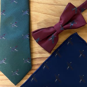 Peut inclure: Un ensemble de trois accessoires assortis avec un motif répété de petits avions. L'ensemble comprend une cravate vert foncé, un nœud papillon bordeaux et un mouchoir de poche bleu foncé.