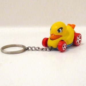 May include: A yellow rubber ducky keychain with red wheels and a silver chain. The ducky has a blue beak and black eyes.