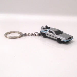 May include: A silver-colored keychain featuring a replica of the DeLorean time machine from the Back to the Future movie. The keychain has a silver metal ring and chain.