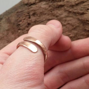 Pu&ograve; includere: Un anello semplice, regolabile, color oro, con una finitura martellata. L'anello &egrave; avvolto attorno a un dito.