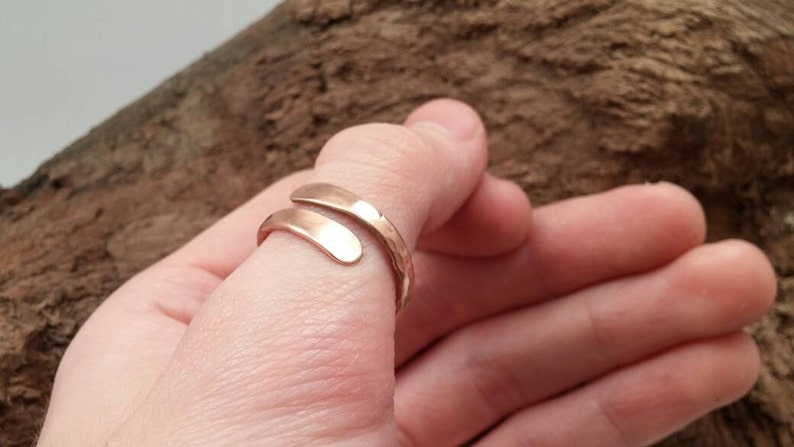 Pu&ograve; includere: Un anello semplice, regolabile, color oro, con una finitura martellata. L'anello &egrave; avvolto attorno a un dito.