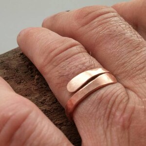 Pu&ograve; includere: Un anello in rame con un design unico e attorcigliato. L'anello &egrave; indossato su un dito di una persona.