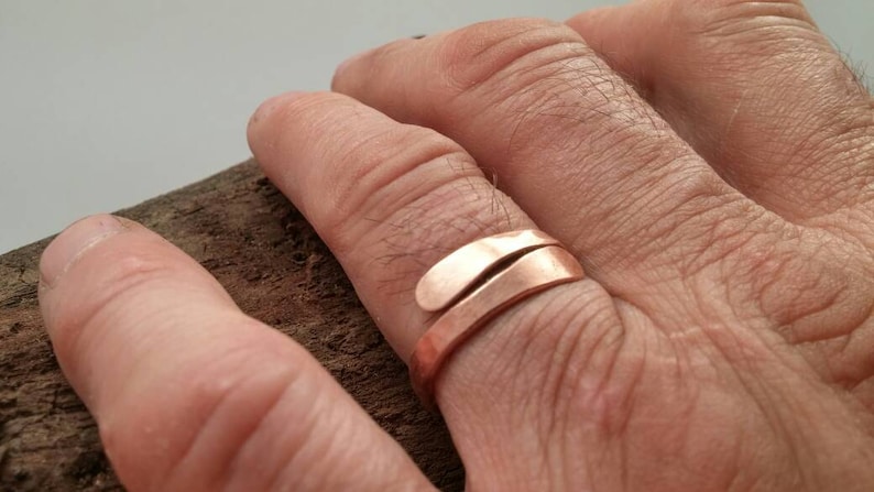 Pu&ograve; includere: Un anello in rame con un design unico e attorcigliato. L'anello &egrave; indossato su un dito di una persona.