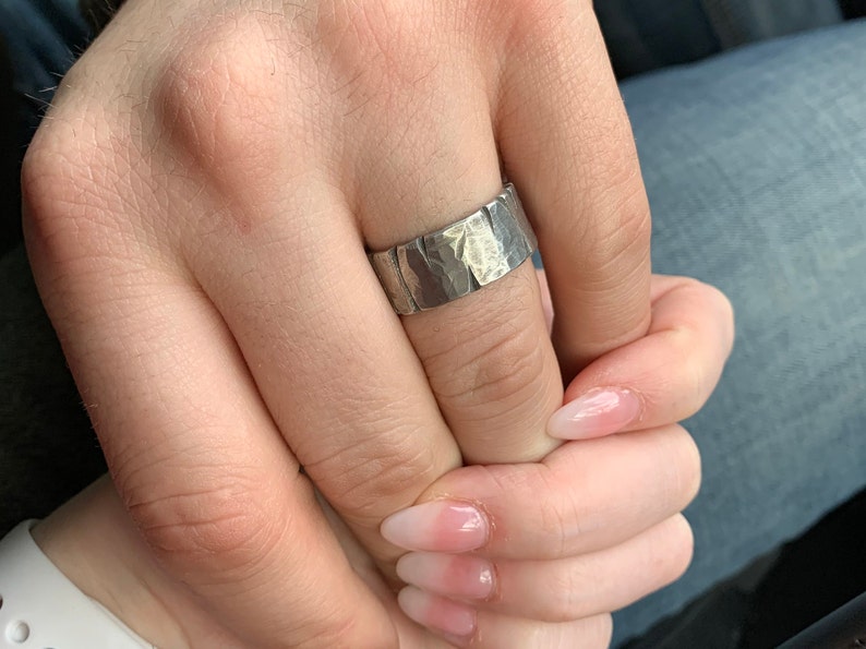 Woman holding mans hand wearing silver pewter Viking ring with battle damage. The band is 10mm wide