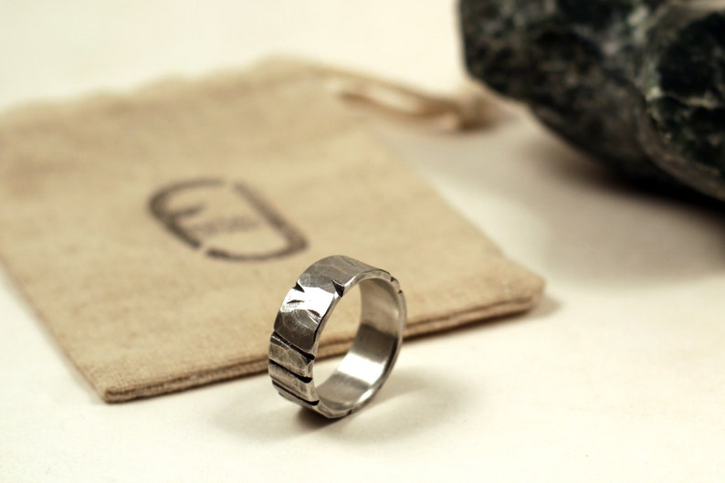 Silver pewter ring 8mm wide with deep cuts and hammered texture sitting next to recycled cotton gift bag stamped with logo
