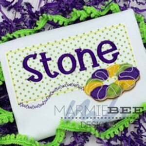 May include: A white shirt with a purple and yellow embroidered design of a donut and the name "Stone" in purple text.