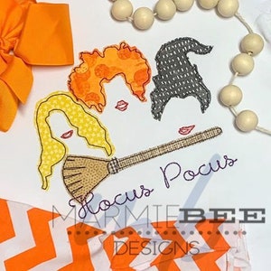 May include: Embroidered design of three witches with a broom and the text "Hocus Pocus" in purple. The witches have orange, yellow, and black hair. The design is on a white background.