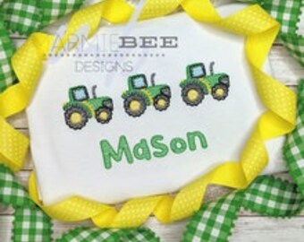 Può includere: Un body bianco con tre trattori verdi ricamati. Il nome "Mason" è ricamato in verde sotto i trattori.