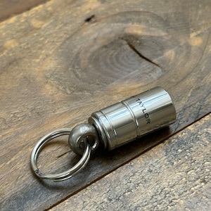 May include: A silver metal keychain with a round ring and a cylindrical charm that says "TAYLOR" engraved on it.