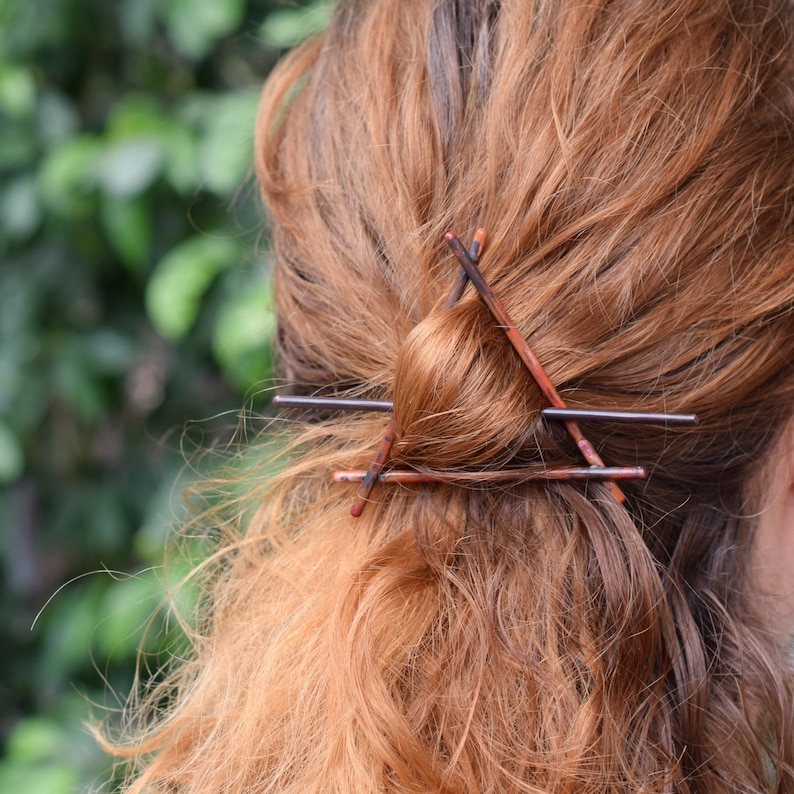 May include: A close-up of a person's hair with a triangle-shaped hair clip made of brown and black metal.