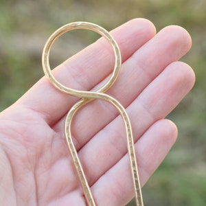 May include: A gold-toned metal hair clip with a hammered finish. The clip is shaped like a figure eight with a loop at the top.