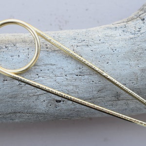 May include: Gold hair stick with a textured finish and a circular loop at one end.