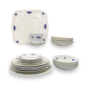 May include: A collection of white porcelain tableware with a blue floral design. The set includes a square serving platter, a teacup and saucer, several plates, and bowls. The plates and bowls are stacked in neat piles.