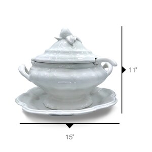 May include: White ceramic soup tureen with a lid and a separate serving spoon. The tureen has a decorative floral design on the lid and a scalloped base. The tureen measures 15 inches wide and 11 inches tall.