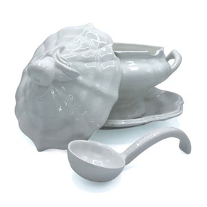 May include: White porcelain gravy boat with a lid and a matching ladle. The lid is shaped like a cabbage and has a detailed design. The gravy boat has a classic shape with a spout and two handles.