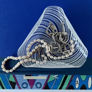 May include: A white and blue glass bowl with a swirl pattern, filled with a pearl necklace and silver horse bit jewelry.