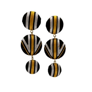 May include: A pair of black and gold statement earrings with three round, layered, geometric patterned discs. The discs are made of woven fabric with a black background and gold stripes.