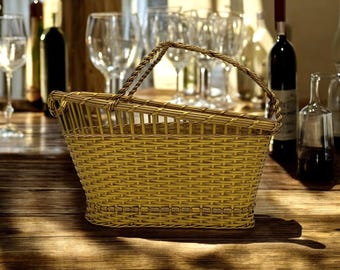 Puede incluir: Una cesta de mimbre tejida con asa, perfecta para transportar botellas de vino. La cesta está sobre una mesa de madera con botellas de vino y vasos en el fondo.