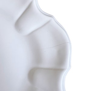 May include: White ceramic plate with a scalloped edge and a small crack. The plate is slightly curved and has a smooth, glossy finish.