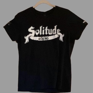 Peut inclure: T-shirt noir avec un imprimé graphique blanc du texte "Solitude Returns" dans une police gothique.