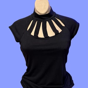 May include: A black short-sleeved shirt with a mock neck and a cutout design at the neckline. The cutout is shaped like a crescent moon and has five vertical strips.