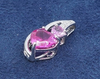 Peut inclure: Un pendentif en argent avec deux pierres précieuses roses en forme de cœur. Le plus grand cœur est d'un fuchsia vif, et le plus petit est rose clair. Le pendentif a un design ajouré décoratif, sur fond bleu.