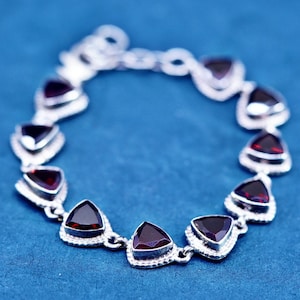 May include: Silver bracelet with triangular, deep red gemstones. The bracelet is made up of linked sections, each holding a gemstone. The gemstones are set in silver-coloured metal with a decorative edge, creating a striking contrast.